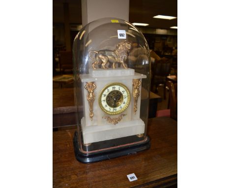 A Victorian mantel clock in alabaster case, with gold painted metal mounts and lion finial, under a rectangular glass dome on