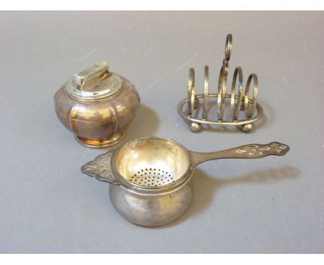 A silver toast rack, a silver tea strainer and holder, and a silver plated table lighter