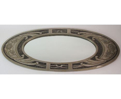 A MARGARET GILMOUR WALL MIRROR of oval shape, the white metal frame decorated with flowerheads and foliage on a hammered blac