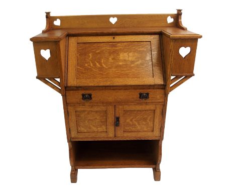 AN ARTS AND CRAFTS OAK WRITING DESK with hinged fall flap enclosing pigeon holes above a drawer, pair of doors and open shelf