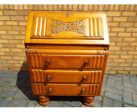 A light oak bureau with carved floral detail, the slope front opening on to automated lopers to reveal a pigeon-hole fitted i