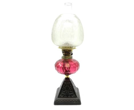 A Victorian oil lamp with cranberry glass facet cut honeycomb effect reservoir, and floral etched glass shade and clear glass