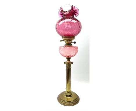 A Victorian oil lamp, the brass base with circular stepped foot supporting a Corinthian modelled column, with cranberry glass