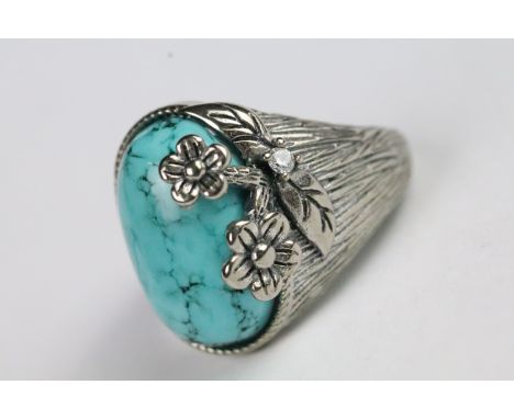 Silver and turquoise ring being set with an oval cabochon to centre with floral detailing and textured shoulders. Marked 925.