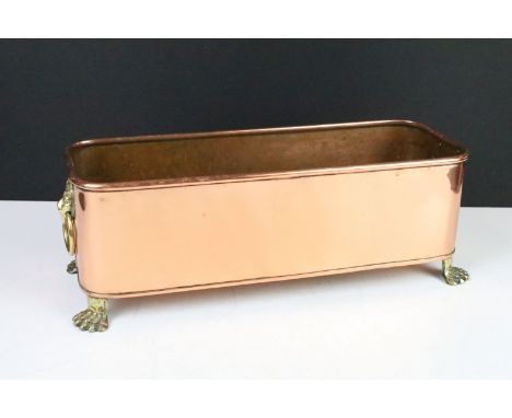 Copper planter with rolled rim and brass lion mask drop ring handles, raised on brass lion paw feet, 39cm long x 13 cm high 