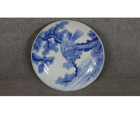 A large Japanese 19th century hand painted blue and white ceramic charger depicting a hawk in a pine tree. Diam.44cm 