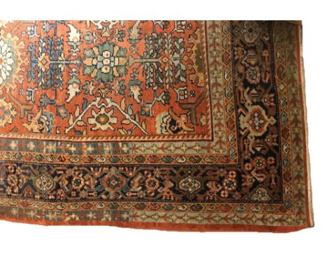 A HERIZ CARPET with repeating floral motif against a terracotta ground, with conforming borders, 348cm x 267cm. Provenance: A