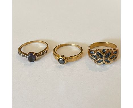 A collection of three 9ct yellow gold gem set rings Featuring a sapphire set flower shape dress ring, size P; a black diamond