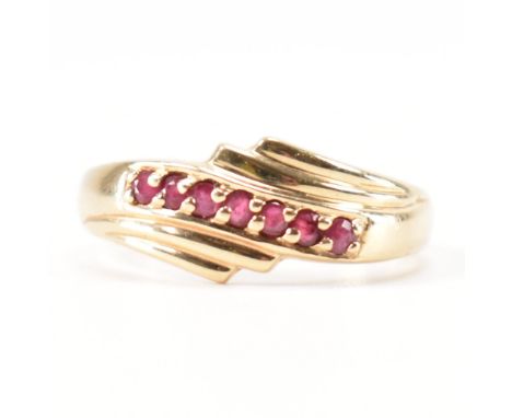 A hallmarked 9ct gold and ruby ring. The ring set with seven round cut rubies in a crossover stylised fan mount to a plain ta