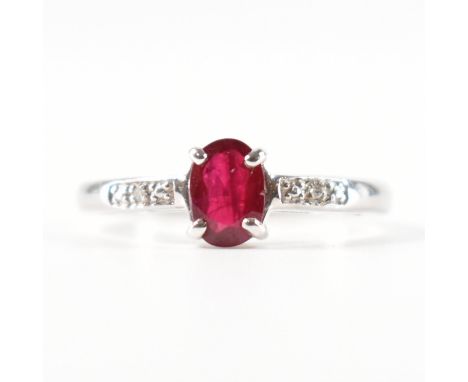 A hallmarked 9ct white gold ruby and diamond ring. The ring set with an oval cut ruby flanked by diamond set shoulders to pla