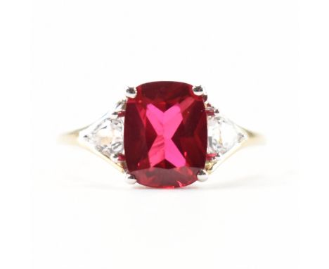 A hallmarked 9ct white gold synthetic ruby and sapphire ring . The ring set with a cushion cut ruby flanked by trilliant cut 