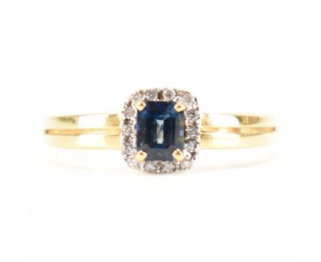 A hallmarked 18ct gold sapphire and diamond halo ring. The ring set with a central step cut sapphire framed by round brillian