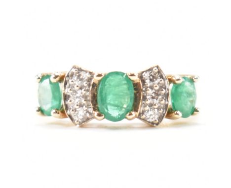 A hallmarked 9ct yellow gold, emerald &amp; diamond ring. The ring having three oval cut prong basket set emeralds spaces by 