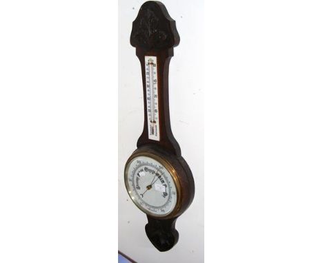 A barometer/thermometer with carved oak surround