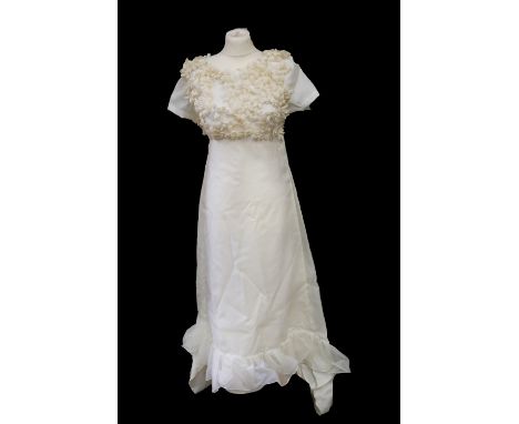A 1971 wedding dress in white nylon, this garment is fully lined with a high waistline, the bodice is decorated in cream flor