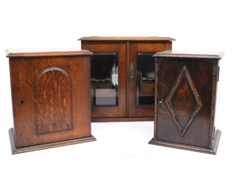 A 20th century oak twin door smokers cabinet, with bevel edged glass doors raised on plinth base, together with two other smo