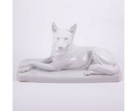 Bohumil Rezl, an Art Deco porcelain study of a dog, modelled reclined on a naturalistic base, blanc de chine glaze, incised s