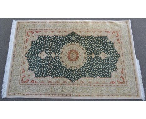 A Persian Isfahan silk carpet, central circular medallion in tones of red, cream and buff on an emerald ground with scrolling