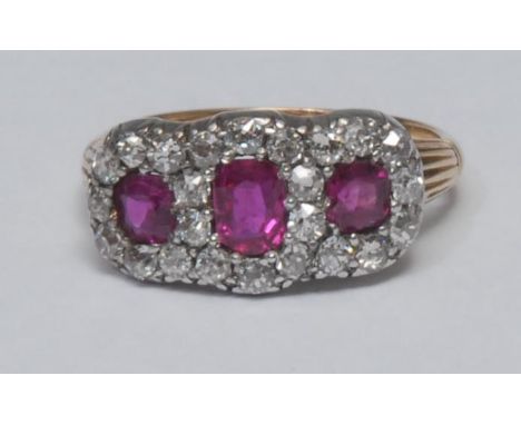 A ruby and diamond cluster ring, central oval vibrant red ruby, flanked by a smaller mixed cut ruby either side, all three su