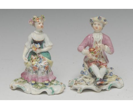 A pair of Derby Patch Mark figure, of a boy and girl, both seated, wearing floral chaplets, holding flower posies, shaped ova