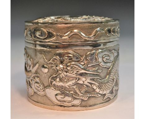 A Chinese silver cylindrical box and cover, chased with ferocious dragons chasing the flaming pearl amongst scrolling clouds,