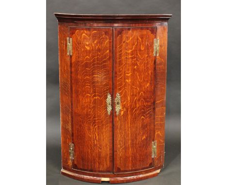 A George III mahogany crossbanded oak bow fronted wall hanging corner cupboard, moulded cornice above a pair of doors enclosi