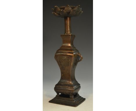 A Chinese bronze candlestick, lotus sconce, vase shaped pillar with scroll handles and cast with panels of trellis, stepped r