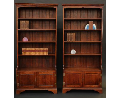 A pair of oak library bookcases, each with dentil cornice above four shelves, the projecting bases with panelled doors, brack
