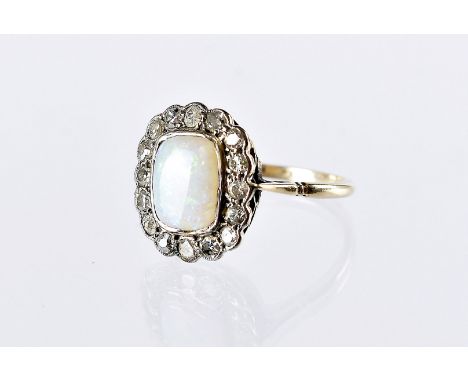 An Art Deco period opal and diamond cluster dress ring, cushion shaped stone surrounded by eight cuts in platinum tablet, on 