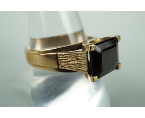 A 9 ct gold and garnet finger ring, the rectangular cut stone set on a broad tapering shank with textured shoulders, R/S, 4.8
