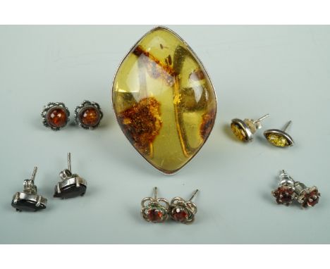 A large asymmetric amber cabochon ring, bezel-set in white metal, stamped 925 and tested as silver, together with garnet and 
