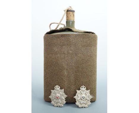 A British army water bottle and two Border Regiment cap badges