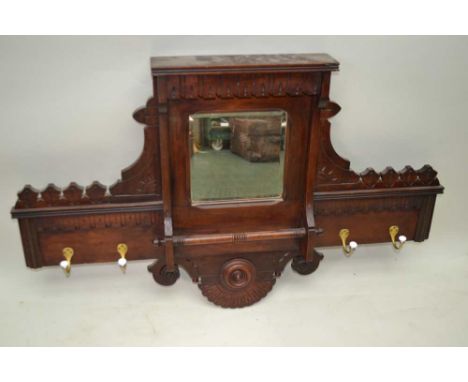 A MAHOGANY FINISHED WALL MOUNTABLE HAT &amp; COAT STAND, having applied carved detailing, insert central bevelled mirror, wit