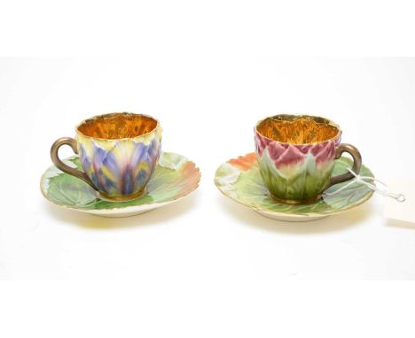 Two floral moulded coffee cups and saucers, variously decorated with moulded flower petals in shades of pink and purple, with