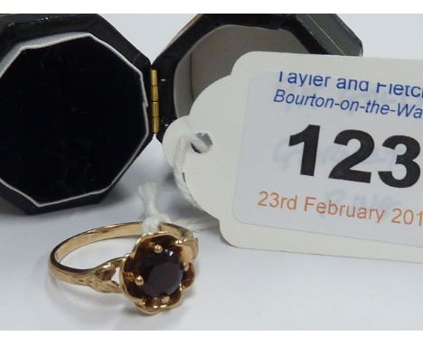 A 9-carat gold ladies ruby Dress Ring, the claw set stone in a floral mount and having floral engraved shoulders, the shank s