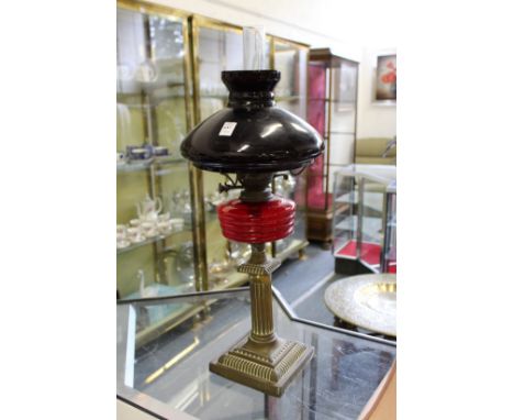 A brass oil lamp with ruby colour brass reservoir and opaque glass shade.