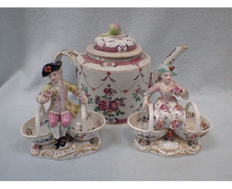 A GUILDED CERAMIC FIGURE SITTING BETWEEN TWO BASKETS another similar and a decorated teapot