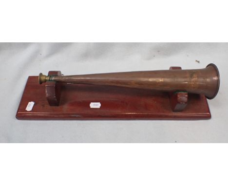 A COPPER HUNTING HORN WITH BRASS MOUTH PIECE with a wooden display base, horn 38cm length 