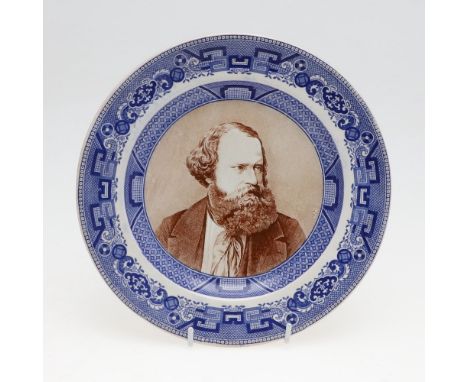 A pottery plate with dished centre with a portrait of Albert Smith in brown, looking to his left, in a blue transfer printed 