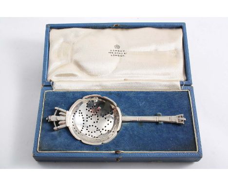 AN ART DECO CORONATION COMMEMORATIVE TEA STRAINER with a stylised crown at each end, by R.E. Stone, London 1935 (in a fitted 