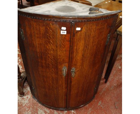 A George III oak bow front hanging corner cupboard with a dentil cornice, the panel doors having mahogany crossbanding, 75cm 