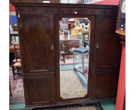 An early 20th century mahogany triple wardrobe, outswept cornice above a central mirrored door flanked by two further panel d