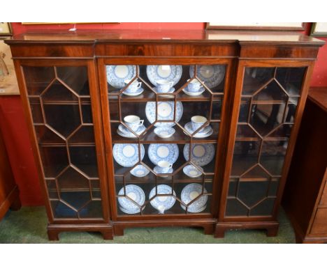A George III style mahogany inverted break-centre bookcase, moulded outswept cornice above a central glazed door enclosing th