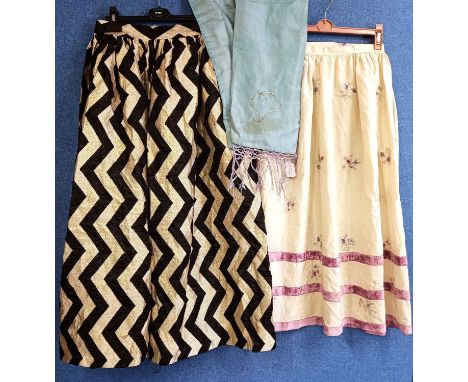 Two skirts, one a custom made black and gold zigzag patterned skirt and a cream silk embroidered skirt with vlevet trim, toge