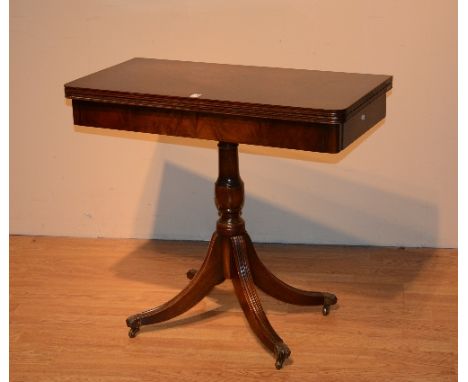 A mahogany folding card table, the swivel top raised above turned column support and reeded downswept supports with brass sab