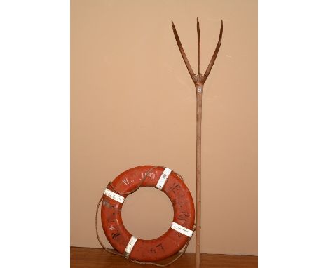A vintage life belt, painted in orange, 74cm diameter, with a wooden three pronged pitch fork, 190cm high (2)