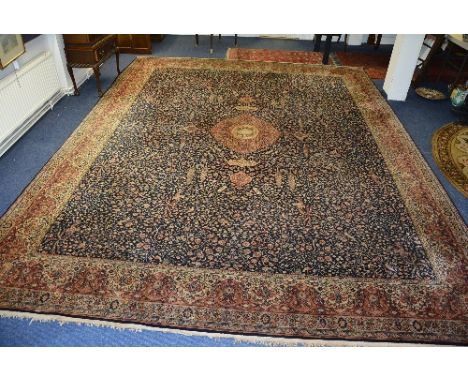 A large Persian style machine made carpet, the green, beige and pink foliate design with bird motif over navy ground, with pi