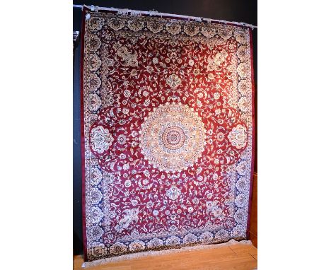 A Keshan style machine made carpet, with gold foliate medallion over red ground, with navy foliate border, 280cm x 200cm