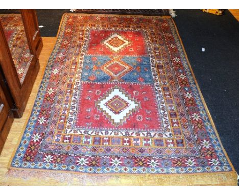 An Eastern carpet, with three central diamonds over green and red panels, with orange, green, red and blue multiple borders, 