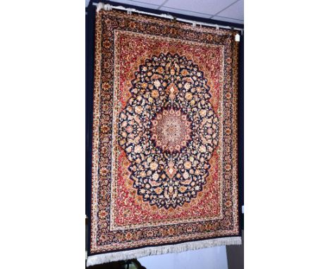 A Keshan style machine made carpet, with central foliate medallion over navy and red ground, with navy foliate border, 230cm 